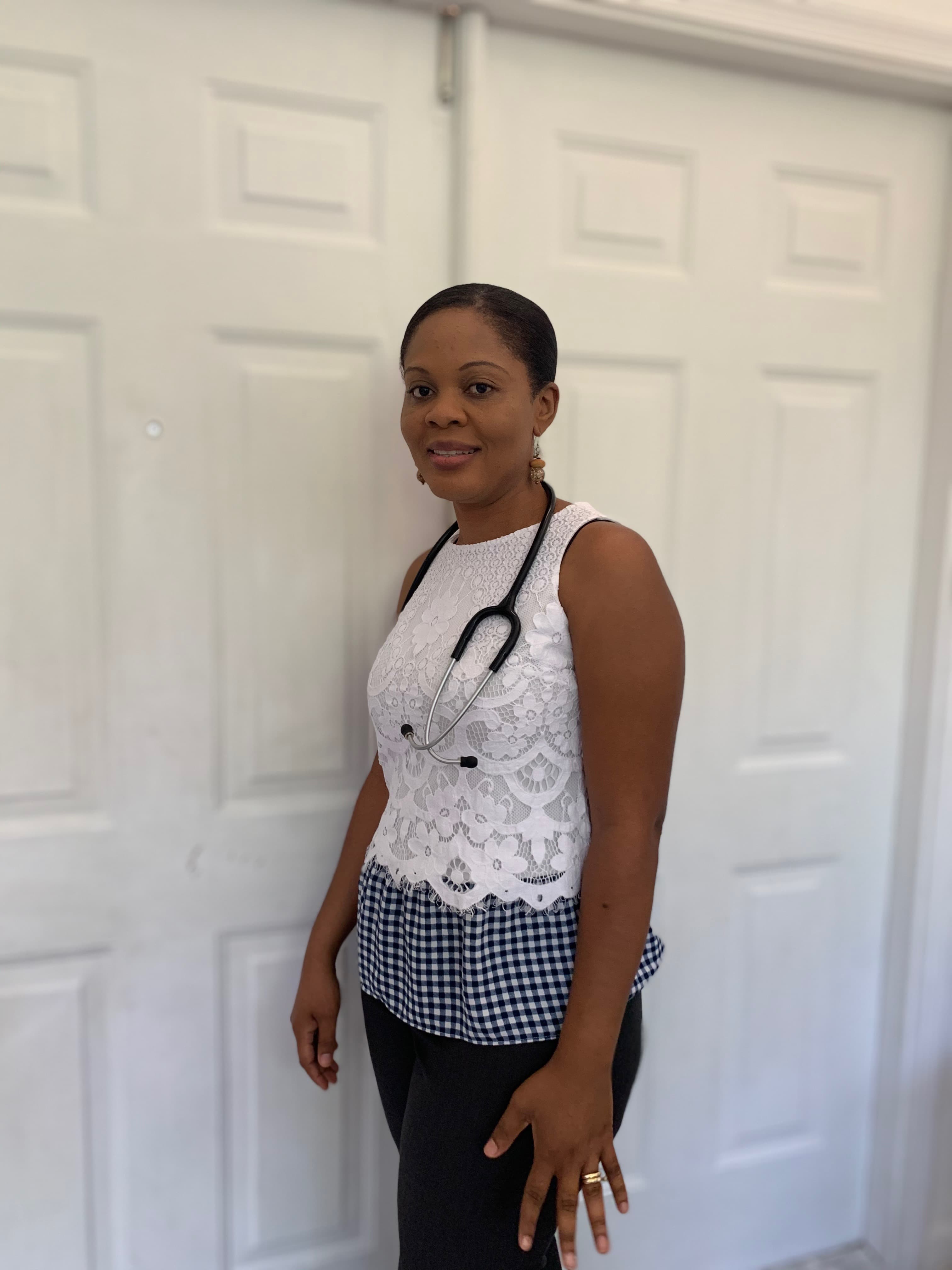 Smiling Black female healthcare professional wearing a white lace top and a stethoscope.