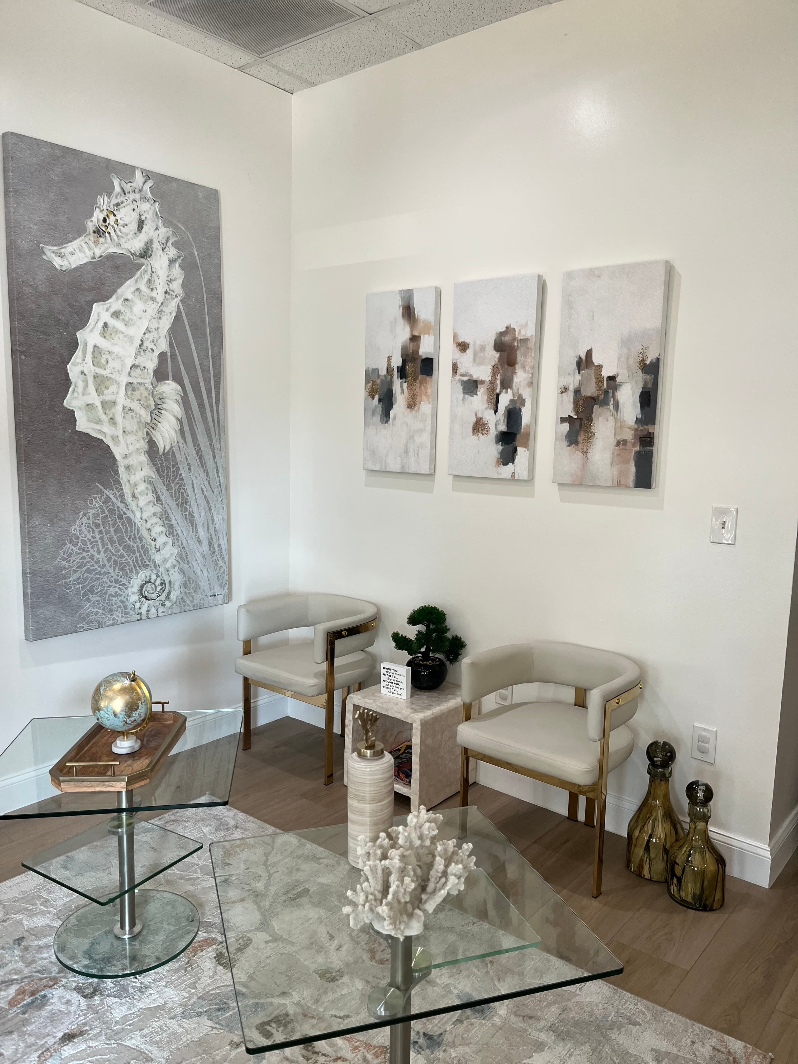 Modern room featuring large seahorse wall art, two white armchairs, and glass coffee tables.