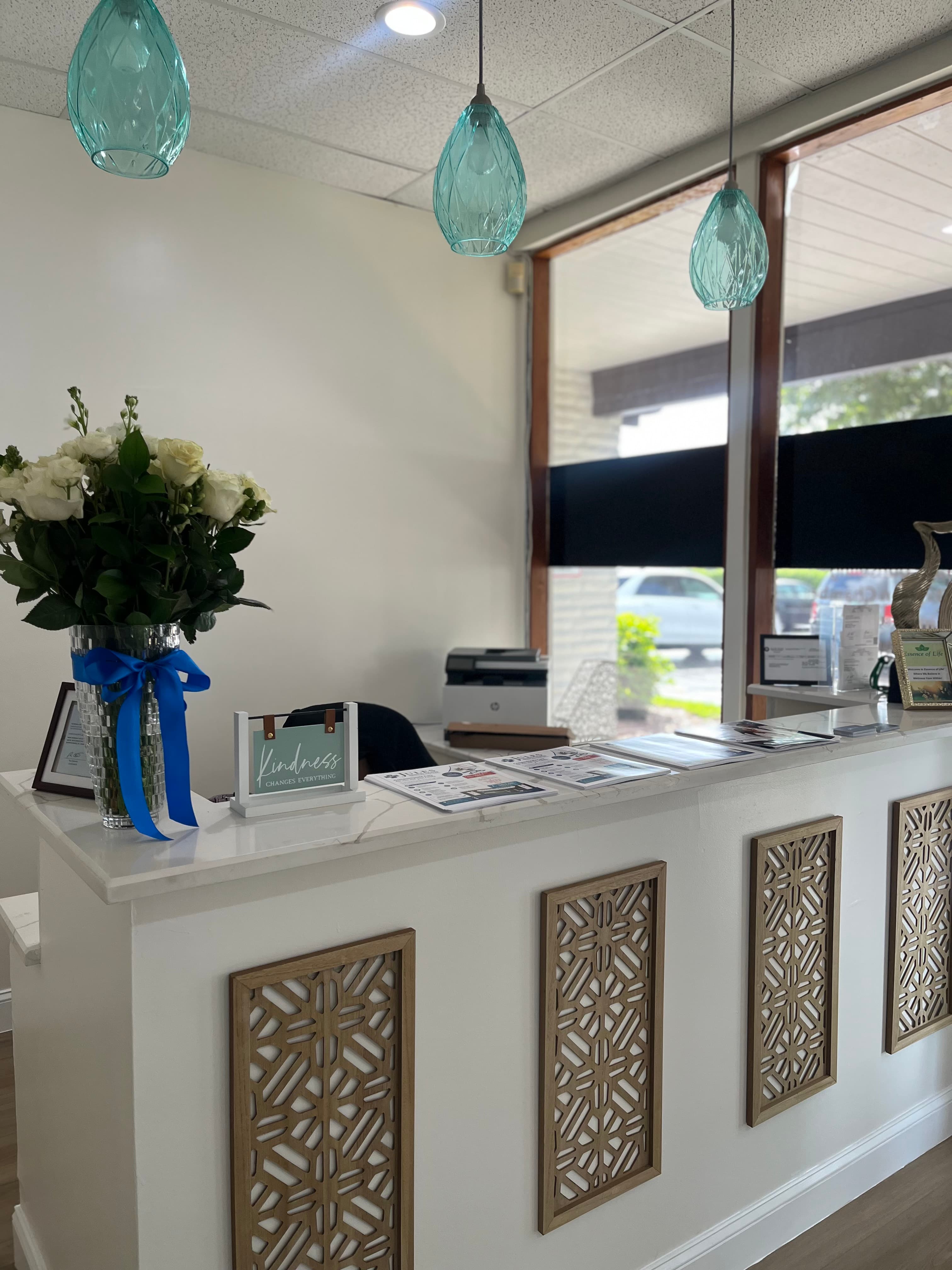 Modern reception desk with white roses, teal glass pendant lights, and a kindness sign.